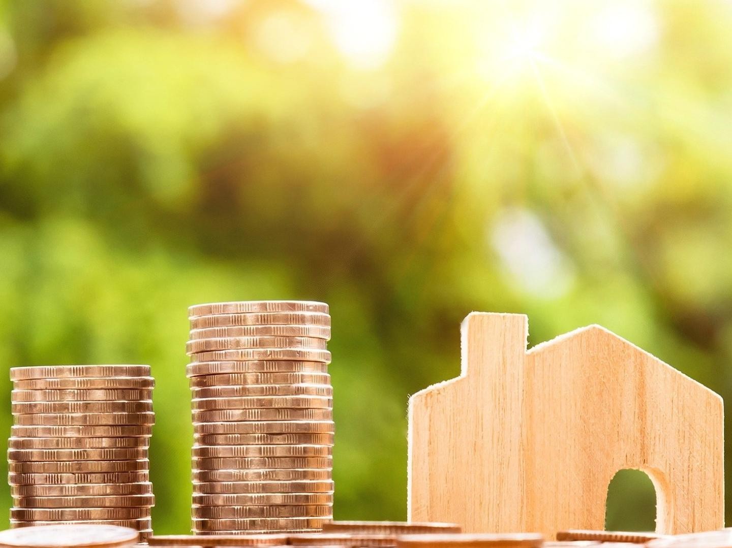 Stapel aus Münzen mit Holzhaus daneben